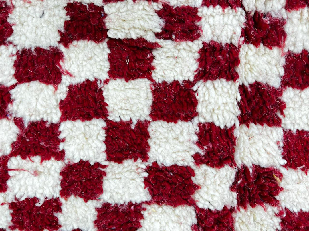Red and white checkerboard Moroccan runner rug made of handmade wool with fringed ends on white background 