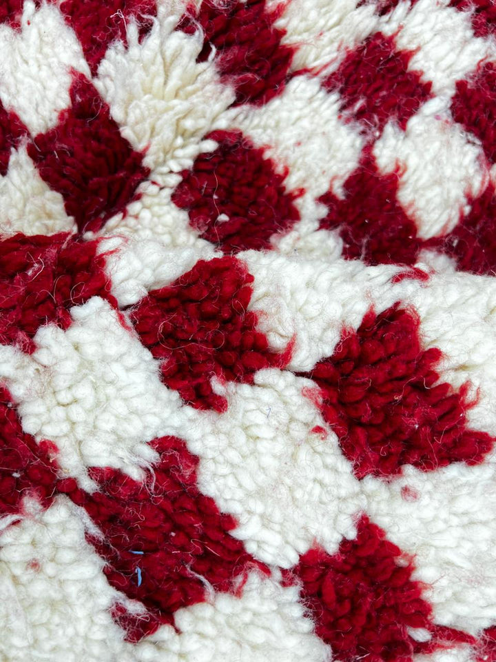 Red and white checkerboard Moroccan runner rug made of handmade wool with fringed ends on white background