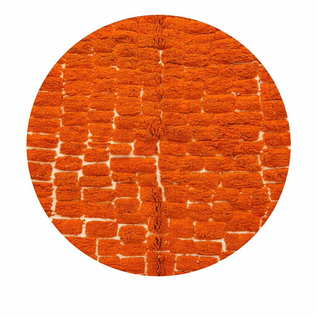 Round orange Moroccan wool shag rug with textured handwoven pattern on white background