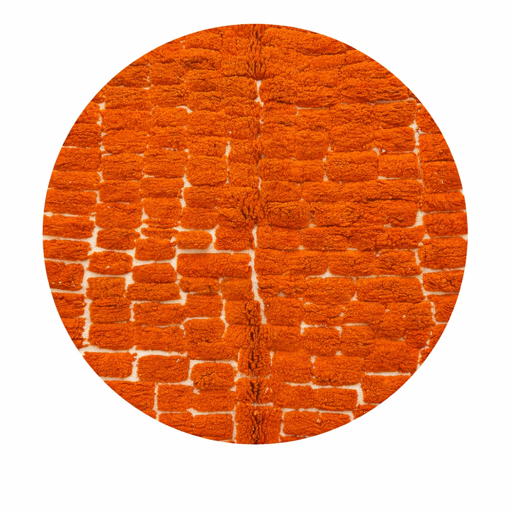 Round orange Moroccan wool shag rug with textured handwoven pattern on white background