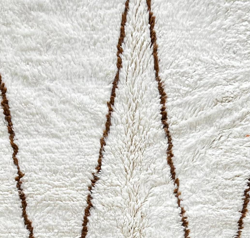 Round Moroccan Berber rug with white wool base and brown hanging geometric motifs, handmade wool carpet
