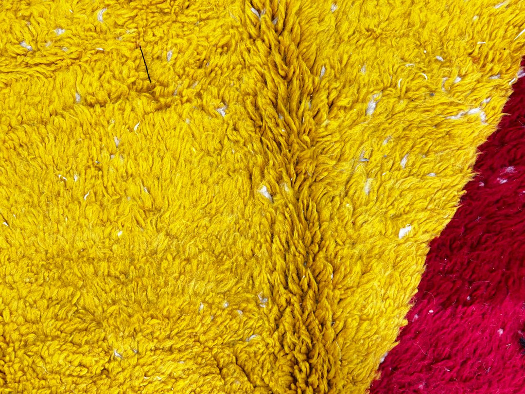 Handmade round Moroccan wool rug with abstract color-block design in blue, cream, yellow, black, and red, featuring a soft shag texture.