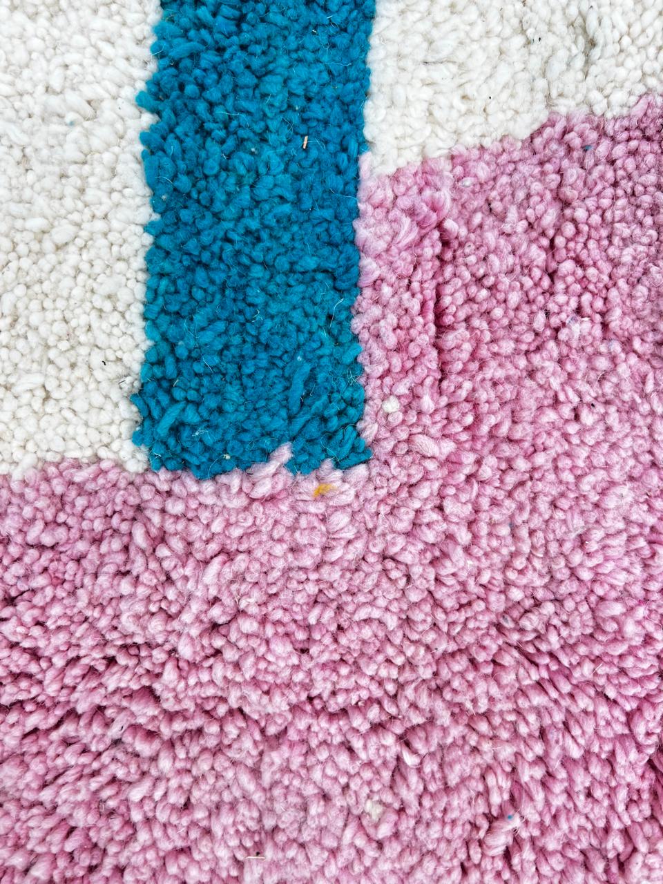 Handmade round Moroccan wool rug with abstract modern design on an white base, featuring orange, black, pink, teal, and beige shapes.