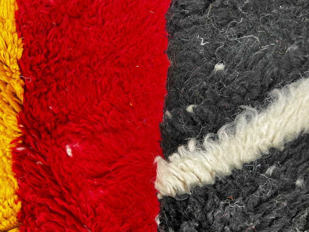 Handmade round Moroccan wool rug with abstract color-block design in blue, cream, yellow, black, and red, featuring a soft shag texture.