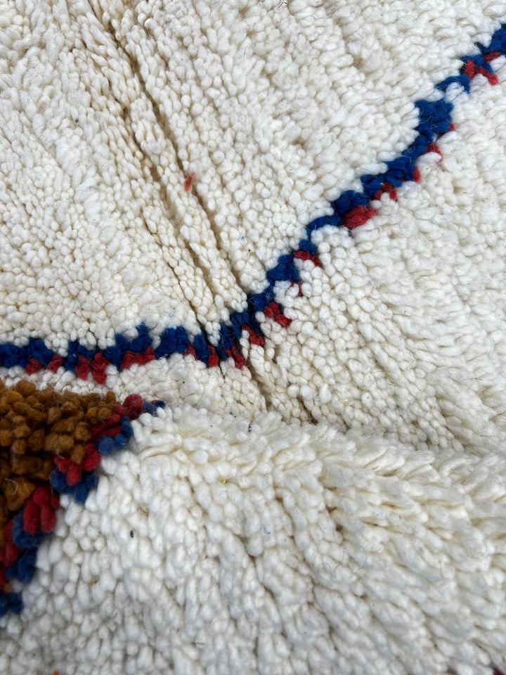 Handmade round Moroccan wool rug with abstract symbolic design, featuring multicolor shapes in blue, red, green, black, and brown on an white base.