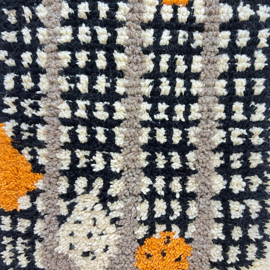 Round black and white Moroccan wool rug with abstract orange Berber motifs and textured grid pattern on white background