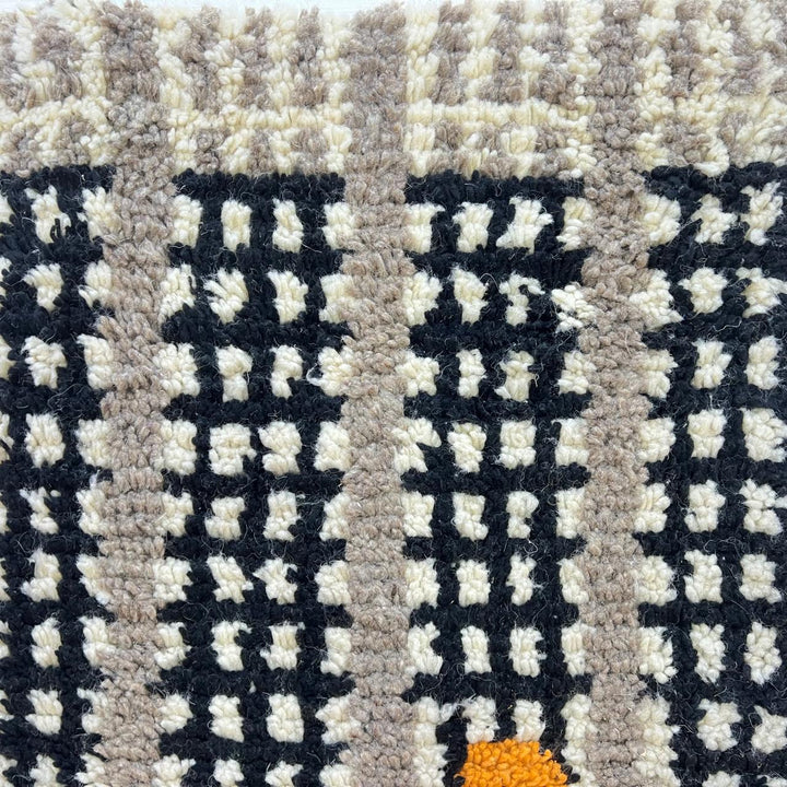 Round black and white Moroccan wool rug with abstract orange Berber motifs and textured grid pattern on white background