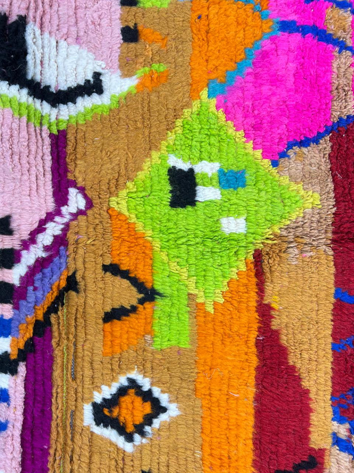 Round Moroccan wool rug with colorful abstract Berber design on pink background