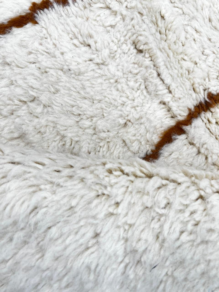 Round Moroccan wool rug with brown geometric lines on white.