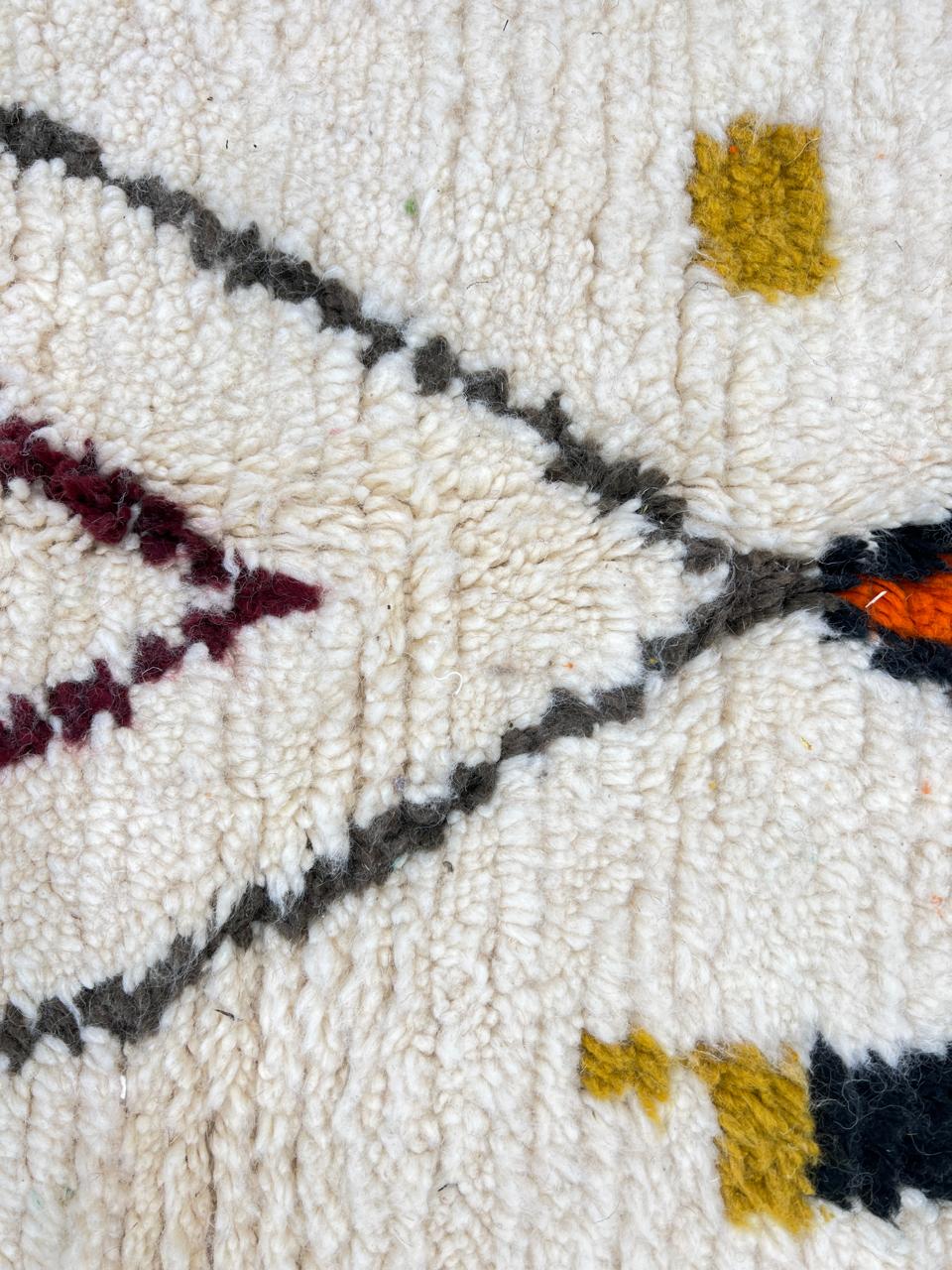 Round Moroccan wool rug with a white base and colorful abstract geometric motifs in orange, mustard, blue, teal, and black.