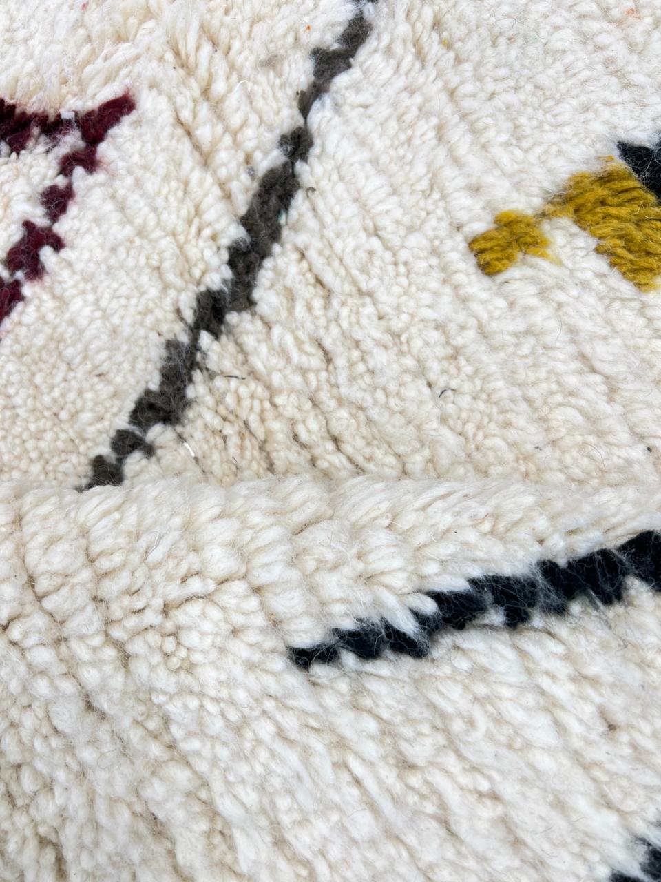 Round Moroccan wool rug with a white base and colorful abstract geometric motifs in orange, mustard, blue, teal, and black.