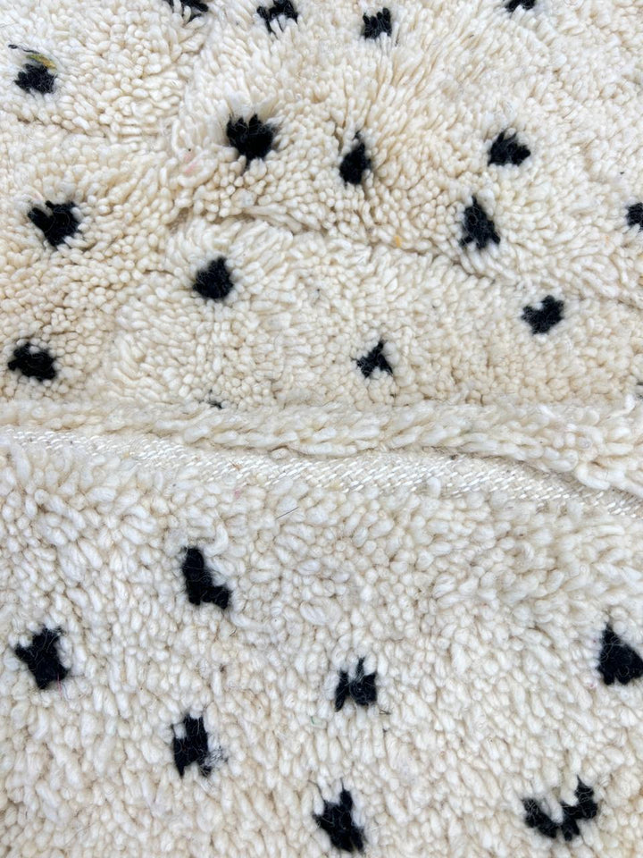 Round white Moroccan wool rug with black dotted motifs and carved diamond pattern