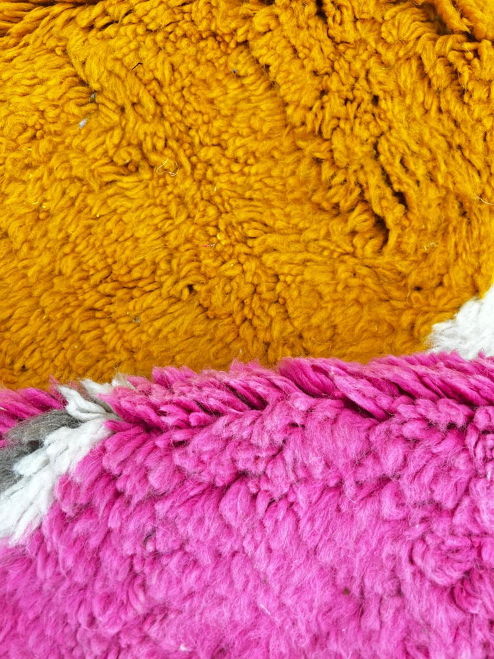 Round Moroccan rug with colorful abstract geometric design in pink, orange, green, grey, and brown on a white base.