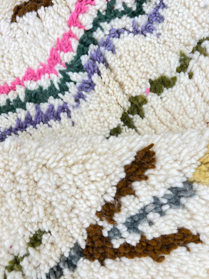 Round Moroccan Berber rug with white wool base and colorful tribal diamond motifs, handmade wool carpet