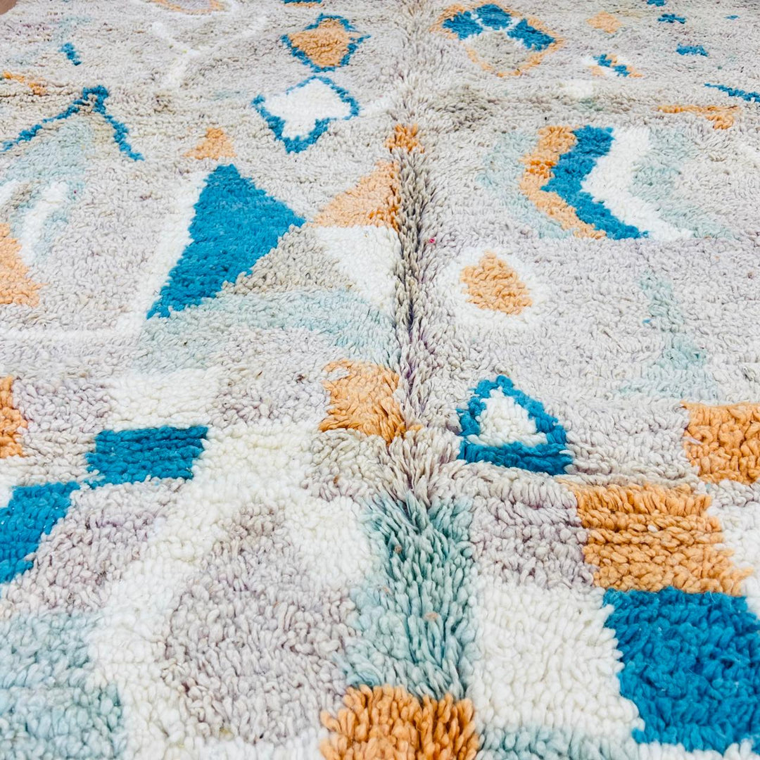Vintage Moroccan wool rug with abstract Berber geometric pattern in beige, blue, and orange tones — handmade tribal carpet from Morocco.
