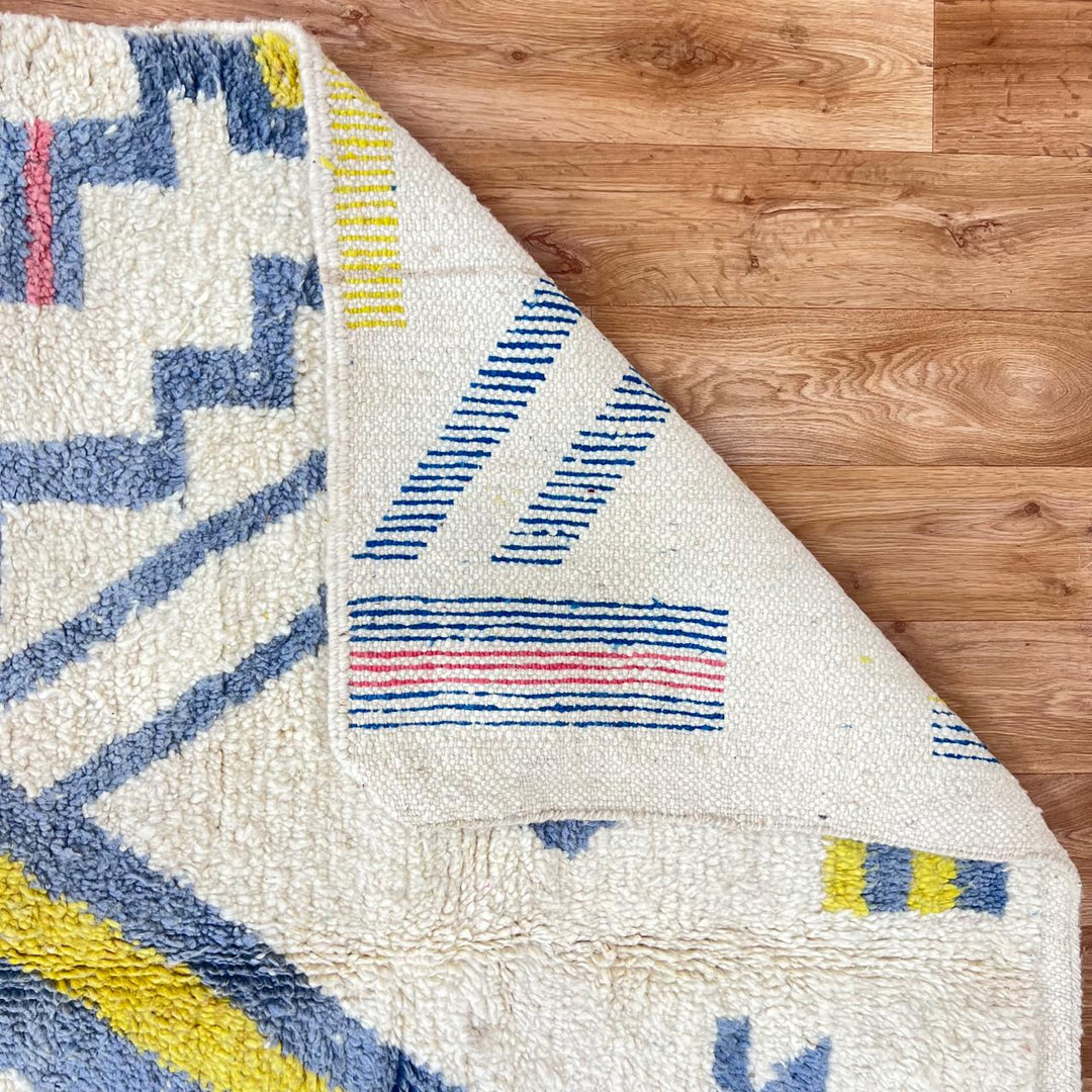 Vintage Moroccan wool rug with ivory base and diagonal geometric patterns in blue, yellow and pink