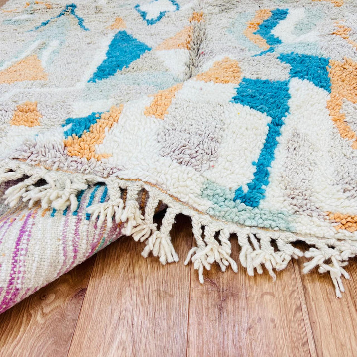 Vintage Moroccan wool rug with abstract Berber geometric pattern in beige, blue, and orange tones — handmade tribal carpet from Morocco.