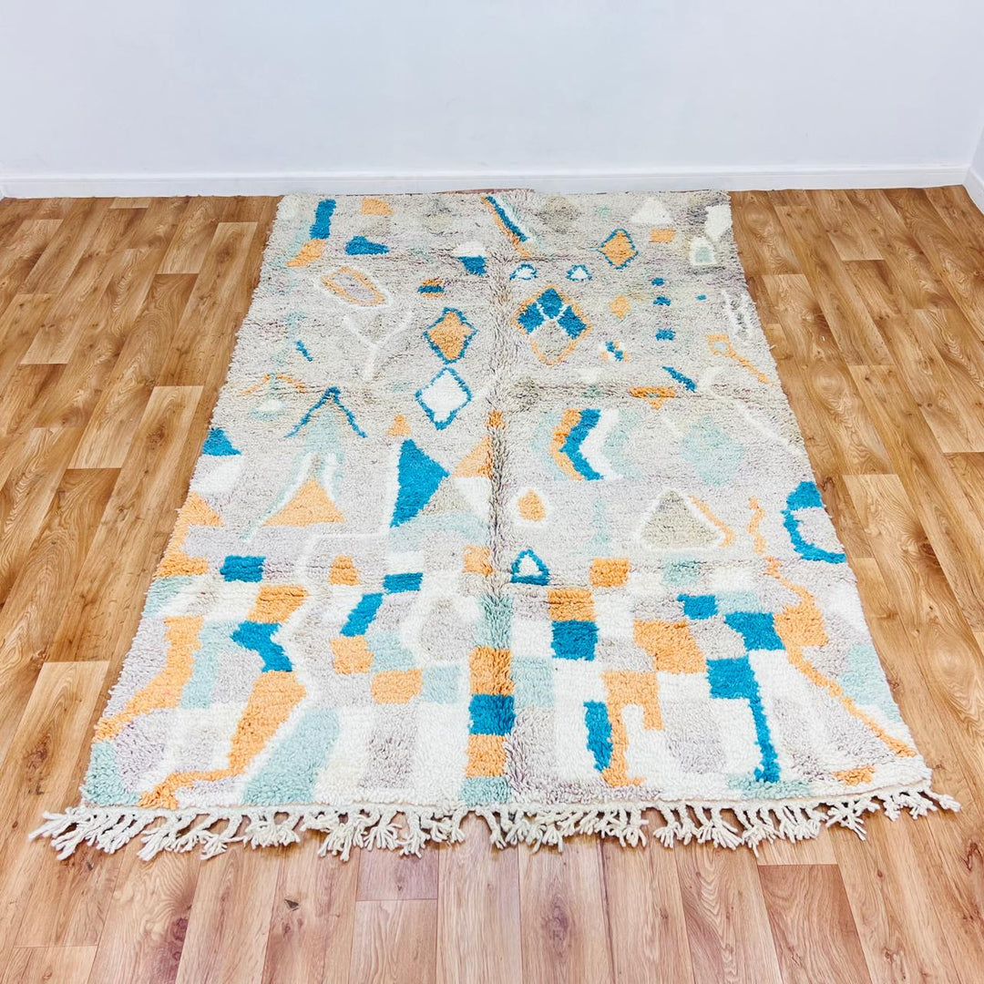 Vintage Moroccan wool rug with abstract Berber geometric pattern in beige, blue, and orange tones — handmade tribal carpet from Morocco.