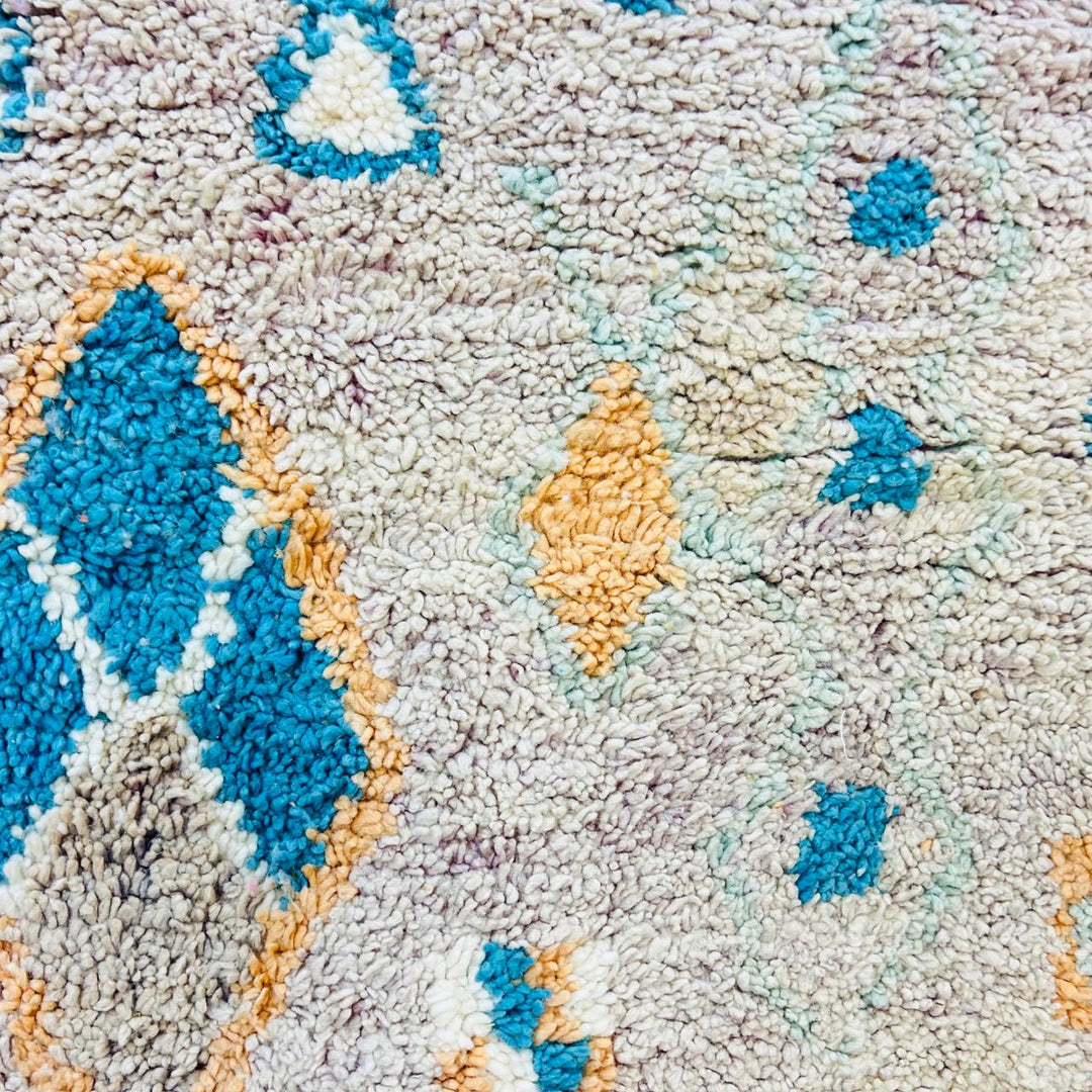 Vintage Moroccan wool rug with abstract Berber geometric pattern in beige, blue, and orange tones — handmade tribal carpet from Morocco.