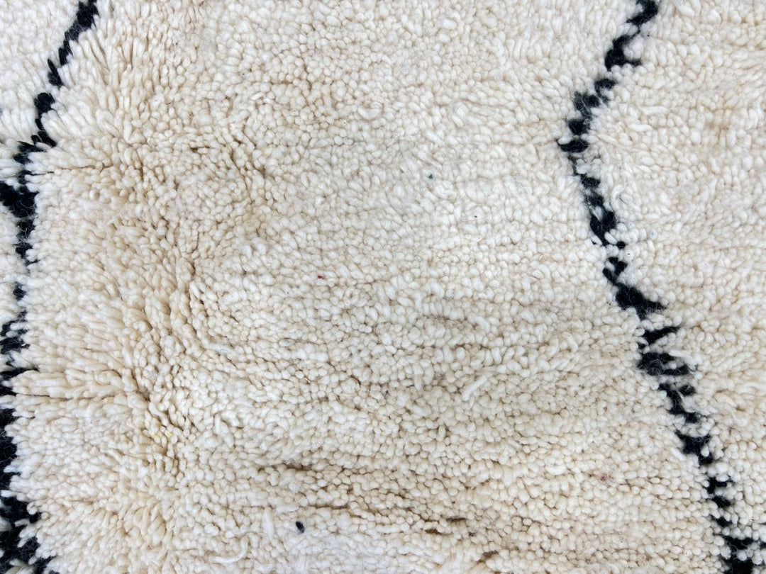 White Moroccan wool rug with black Berber diamond motifs in a round Beni Ourain style.