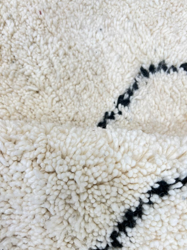 White Moroccan wool rug with black Berber diamond motifs in a round Beni Ourain style.
