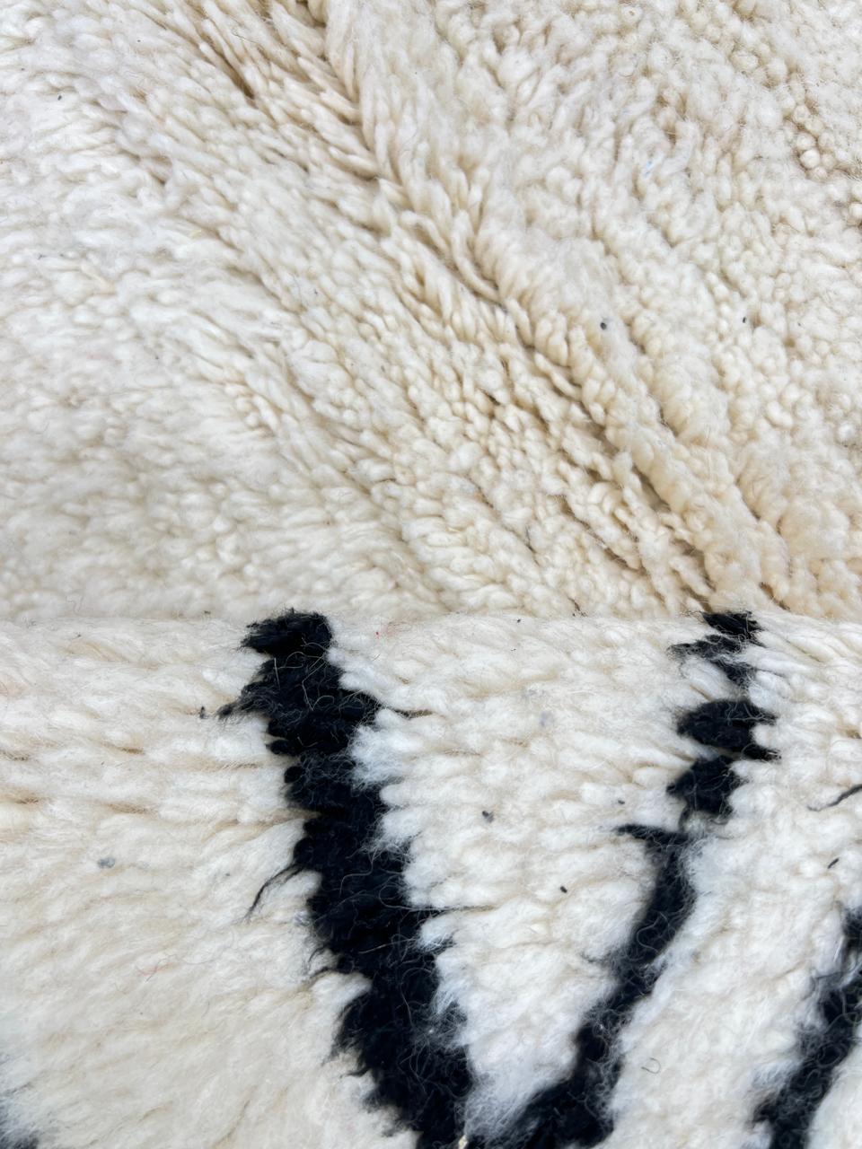 Round white Moroccan wool rug with black Berber diamond motifs in a minimalist design.