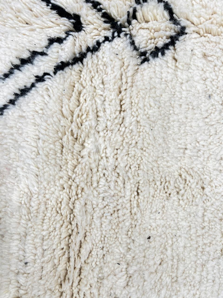 Round white Moroccan wool rug with black Berber diamond motifs in a minimalist design.