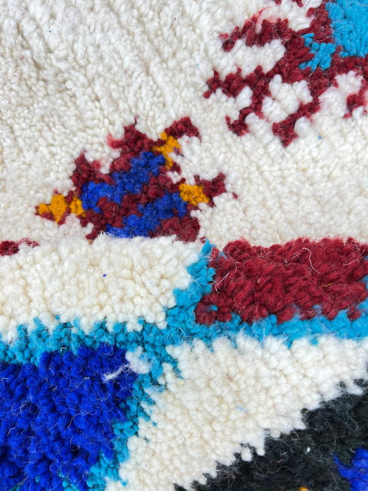 Handmade white Moroccan wool runner rug with colorful tribal Berber motifs in blue, red, yellow, turquoise, and orange