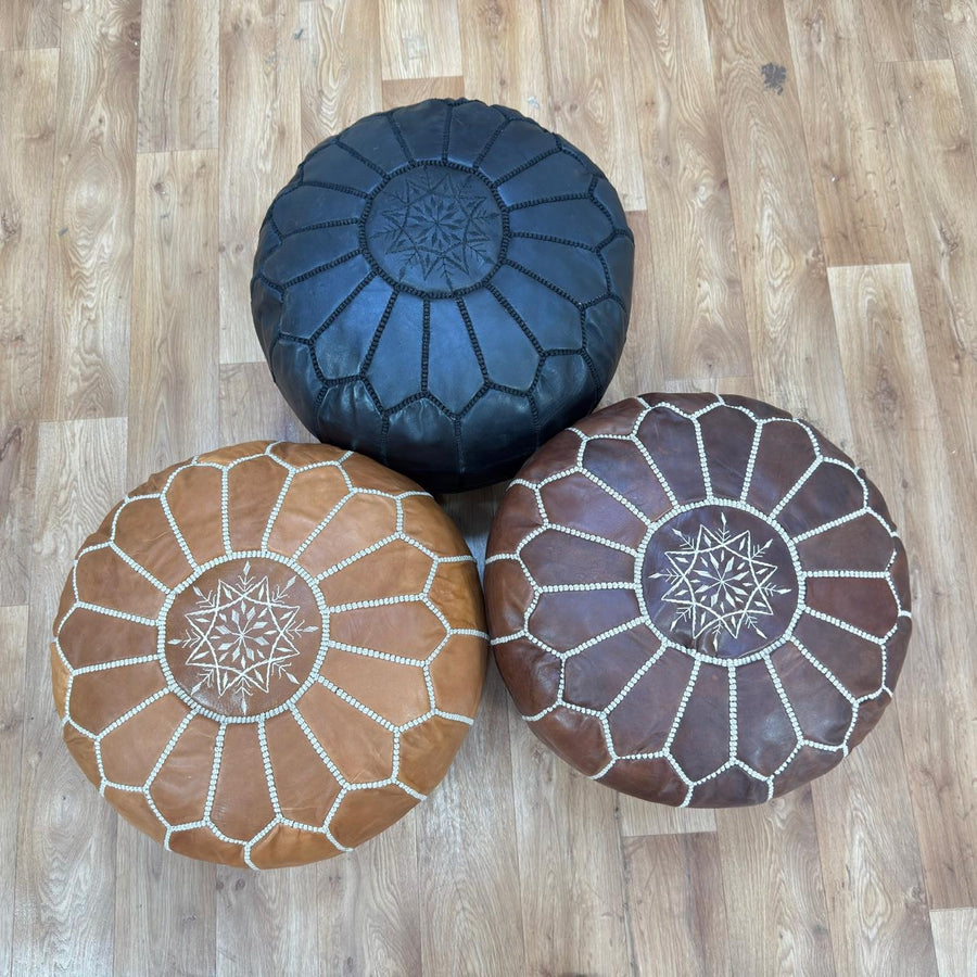 Three leather ottomans in black, brown, and red on a wooden floor.