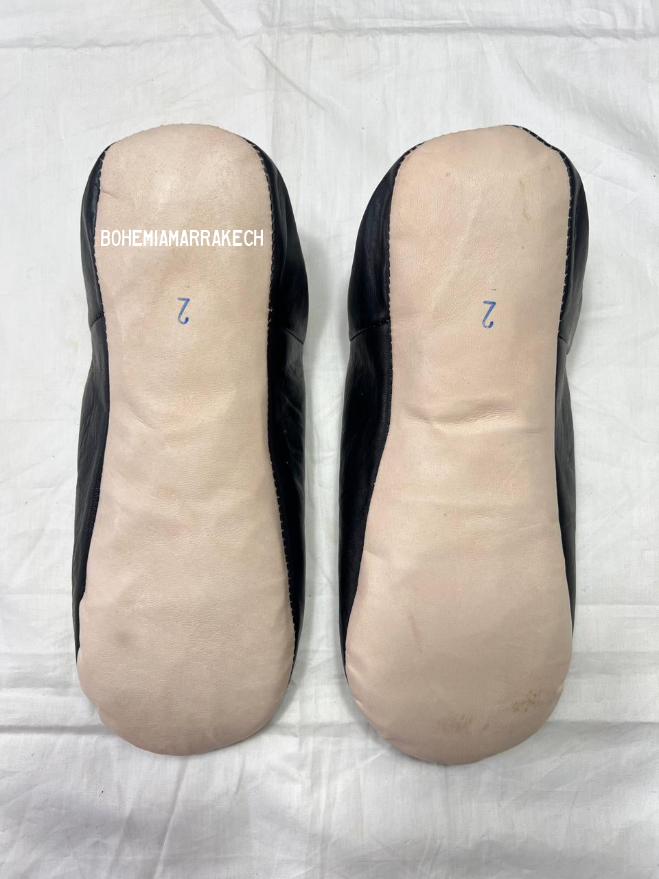 Hand-stitched black Moroccan leather babouche slippers with carved geometric design on soft yellow background