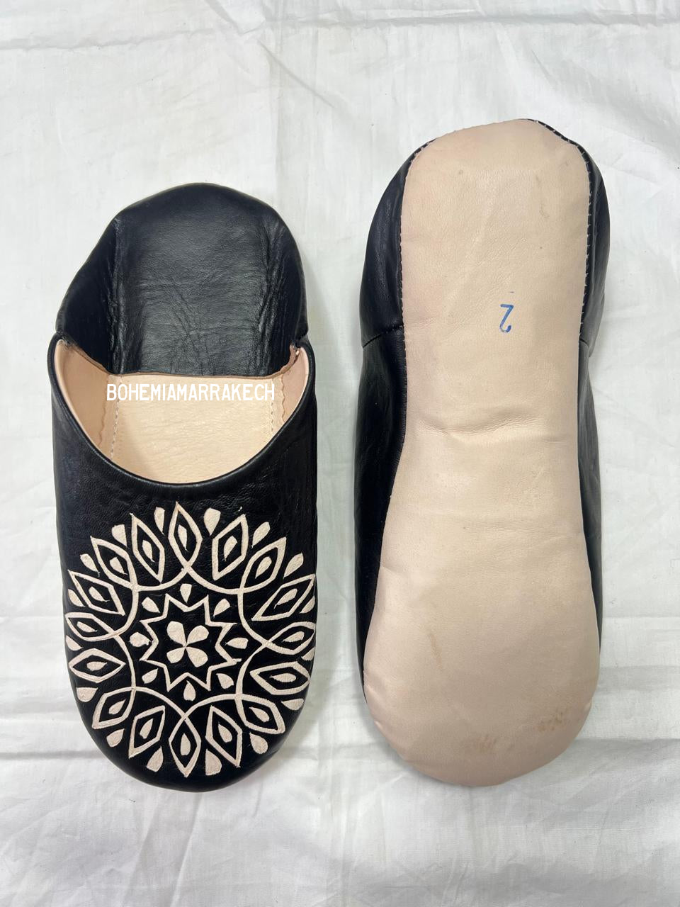 Hand-stitched black Moroccan leather babouche slippers with carved geometric design on soft yellow background