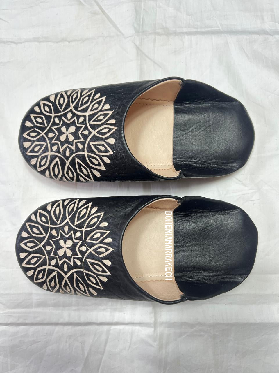 Hand-stitched black Moroccan leather babouche slippers with carved geometric design on soft yellow background