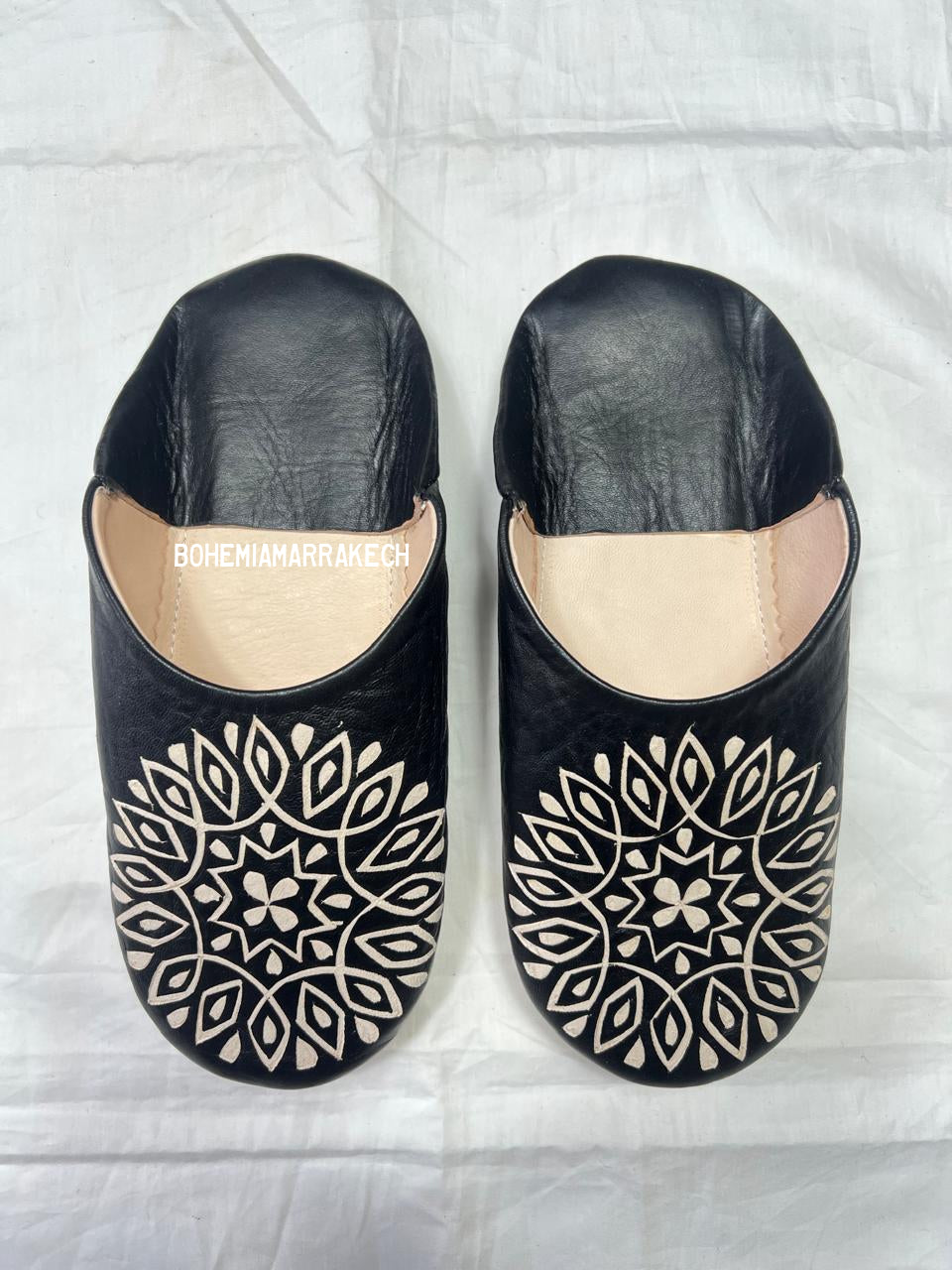 Hand-stitched black Moroccan leather babouche slippers with carved geometric design on soft yellow background