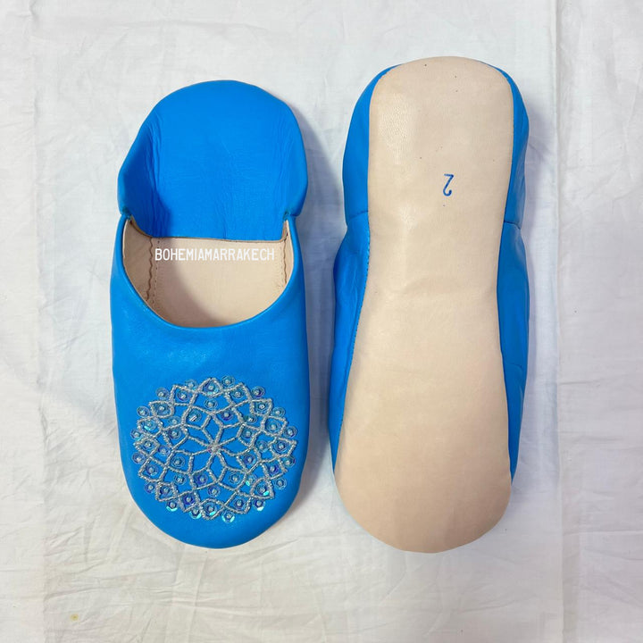 Traditional Moroccan leather babouche slippers in blue, featuring artisan beaded medallion design.