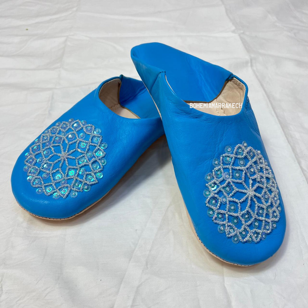 Traditional Moroccan leather babouche slippers in blue, featuring artisan beaded medallion design.