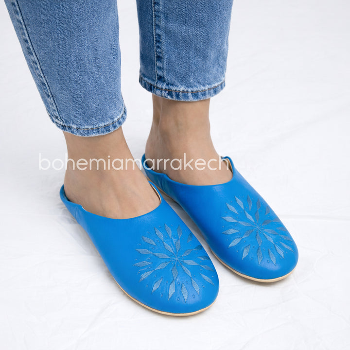 Blue Moroccan babouche slippers with stitched geometric leather design on white background