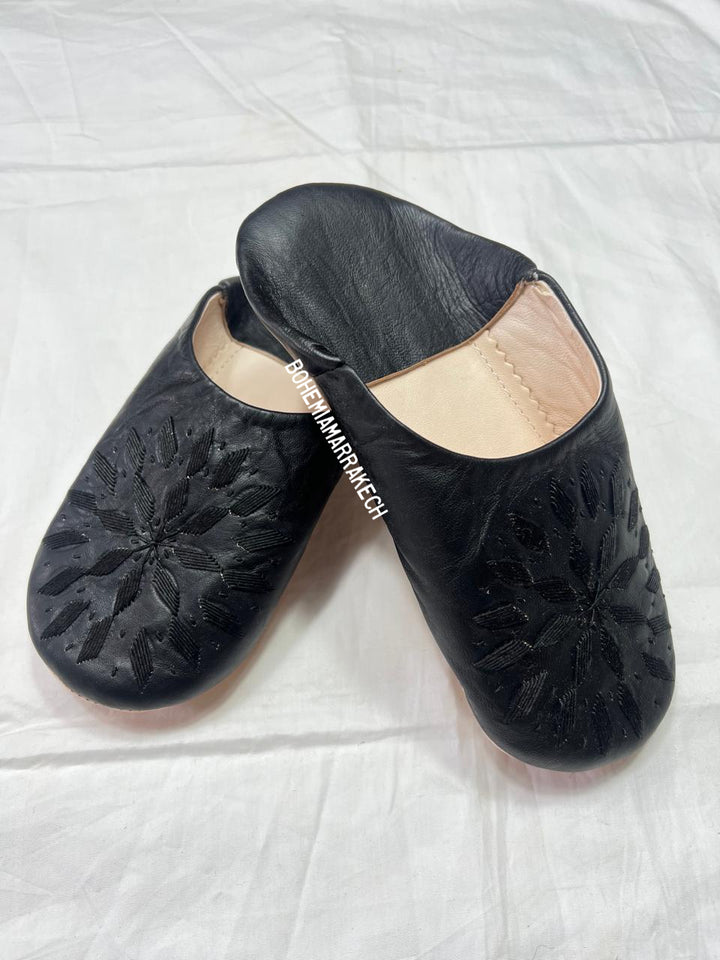 Black Moroccan babouche slippers with stitched geometric leather design on white background