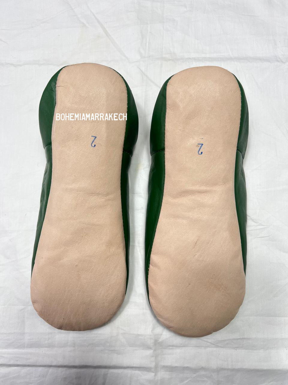 Handmade green Moroccan babouche slippers with stitched leather and carved traditional pattern on a white background