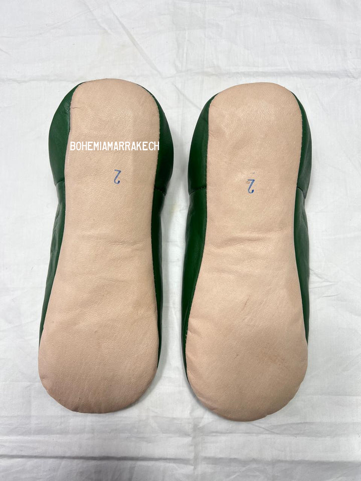 Handmade green Moroccan babouche slippers with stitched leather and carved traditional pattern on a white background