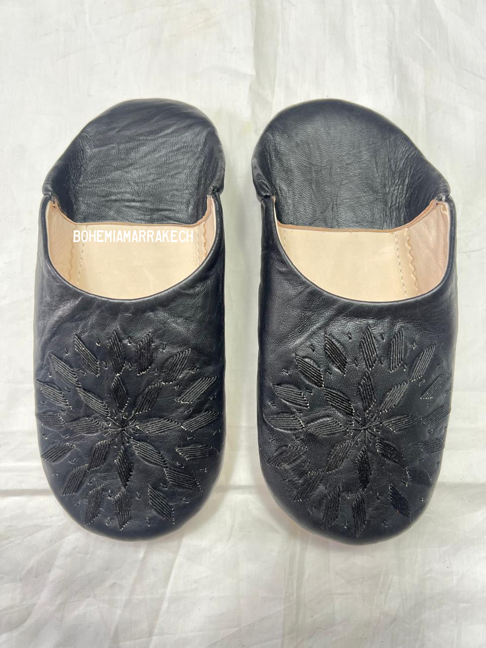 Black Moroccan babouche slippers with stitched geometric leather design on white background