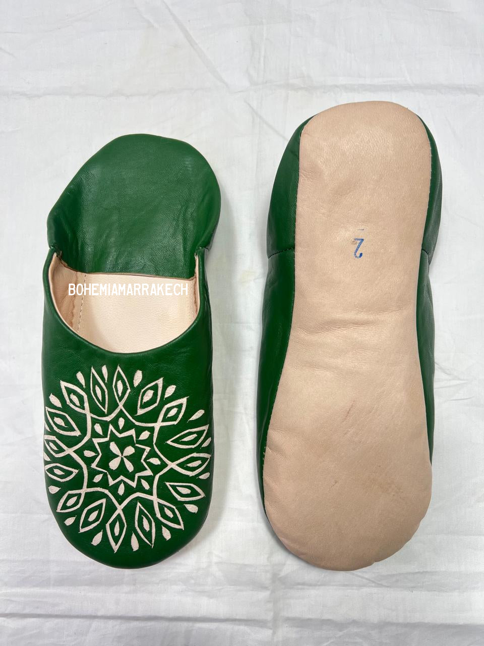 Handmade green Moroccan babouche slippers with stitched leather and carved traditional pattern on a white background