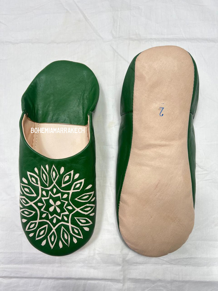 Handmade green Moroccan babouche slippers with stitched leather and carved traditional pattern on a white background