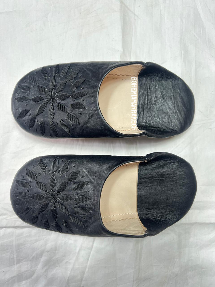 Black Moroccan babouche slippers with stitched geometric leather design on white background