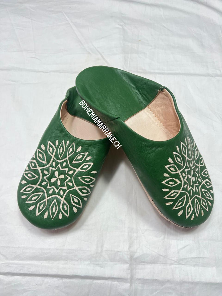 Handmade green Moroccan babouche slippers with stitched leather and carved traditional pattern on a white background