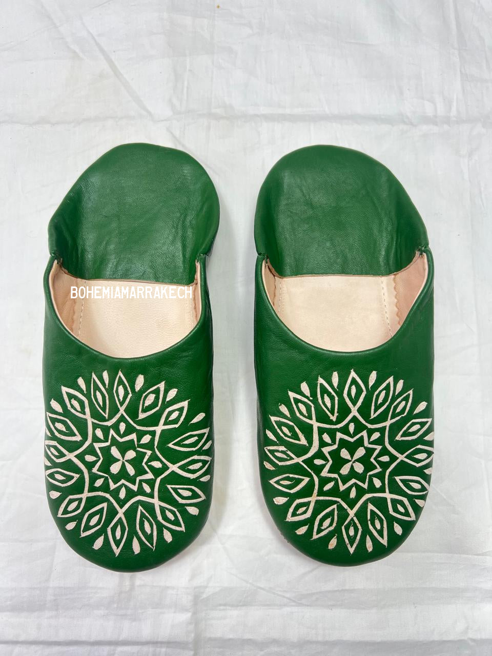 Handmade green Moroccan babouche slippers with stitched leather and carved traditional pattern on a white background