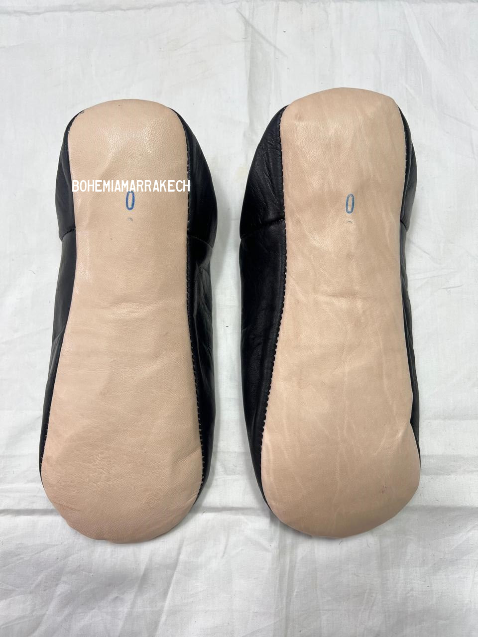 Black Moroccan babouche slippers with stitched geometric leather design on white background