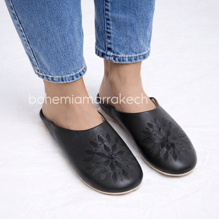 Black Moroccan babouche slippers with stitched geometric leather design on white background