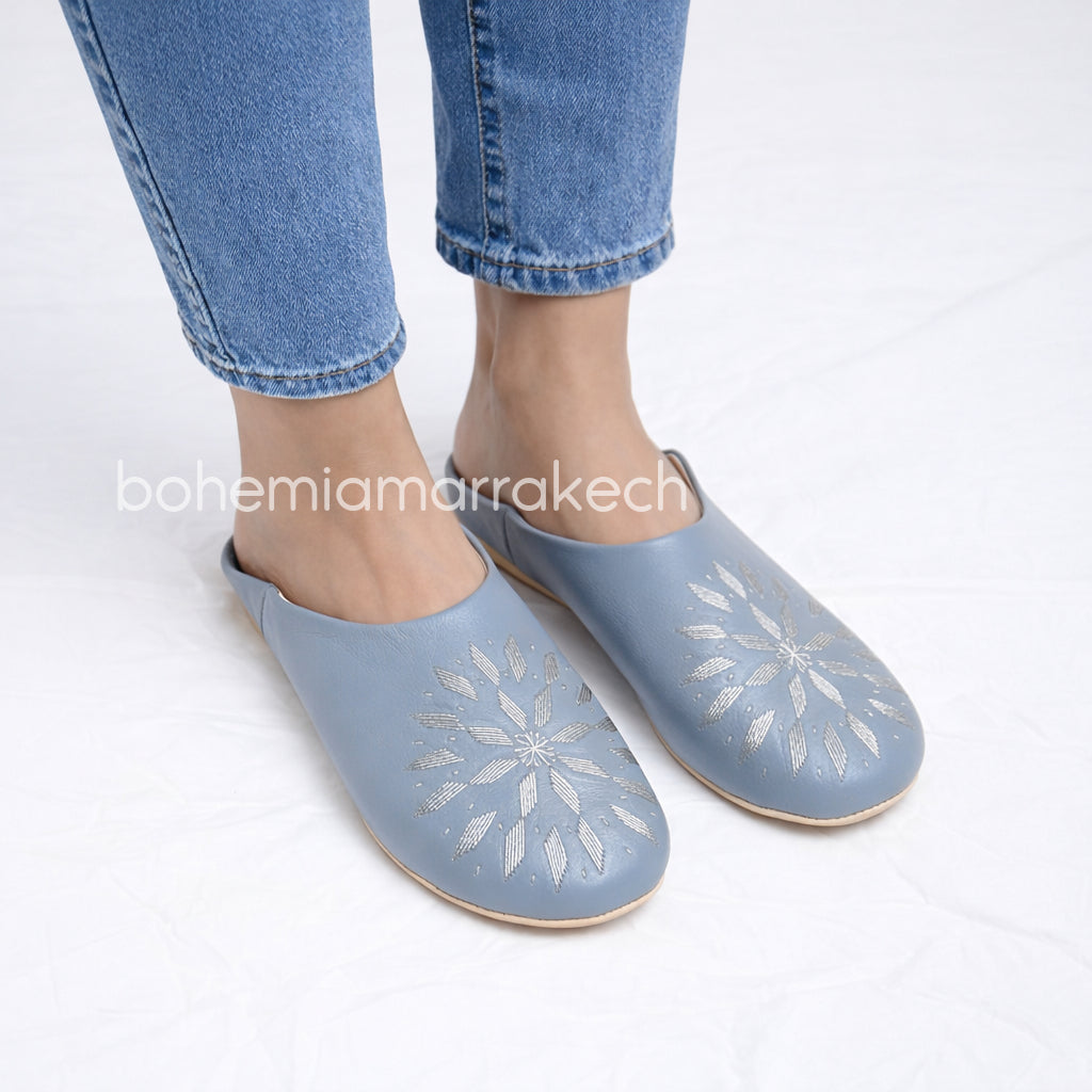 Light gray Moroccan babouche slippers with stitched geometric leather design on light yellow background
