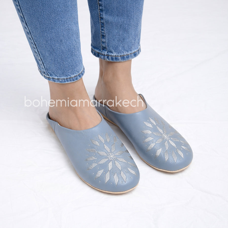 Light gray Moroccan babouche slippers with stitched geometric leather design on light yellow background