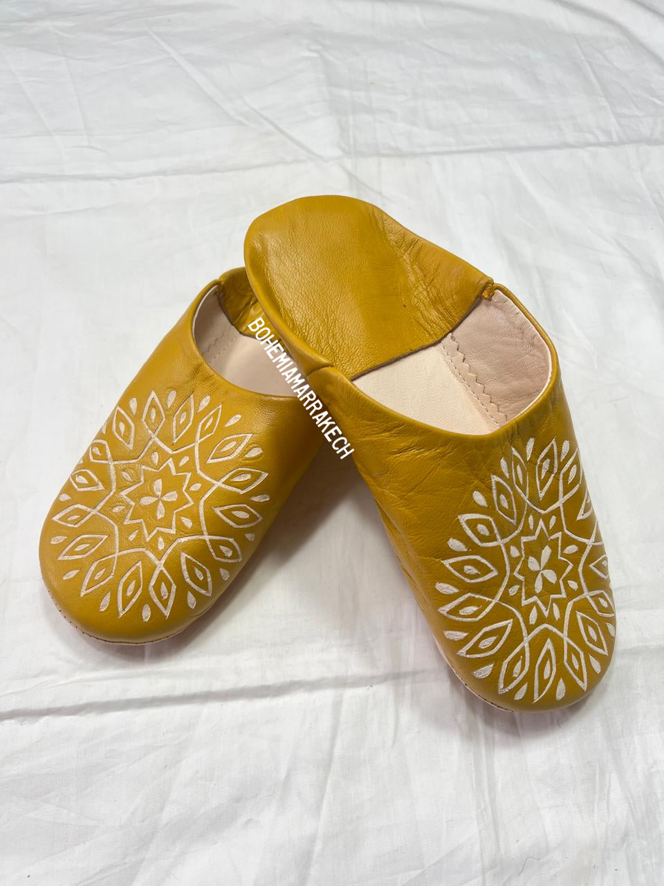 Mustard yellow Moroccan babouche slippers with carved geometric leather design on white background